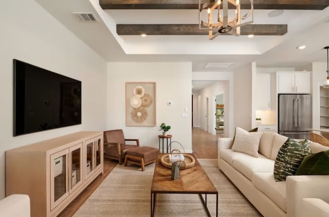 living room with a notable chandelier, beamed ceiling, a tray ceiling, and light hardwood / wood-style floors