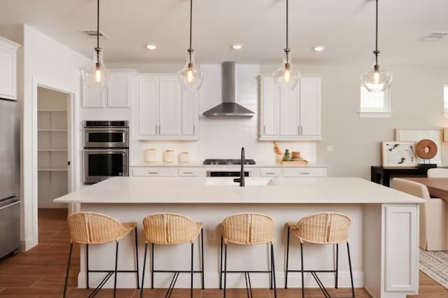 kitchen with white cabinets, a center island with sink, wall chimney exhaust hood, and stainless steel appliances