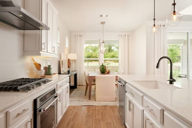 kitchen featuring appliances with stainless steel finishes, a healthy amount of sunlight, wall chimney range hood, and white cabinetry