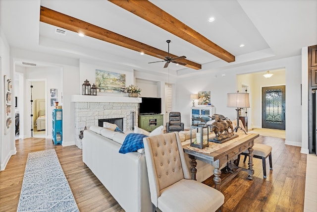 living room featuring beam ceiling, light wood-type flooring, a stone fireplace, and ceiling fan