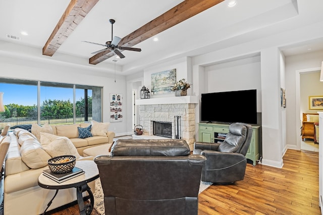 living room with beam ceiling, a stone fireplace, ceiling fan, and light hardwood / wood-style flooring