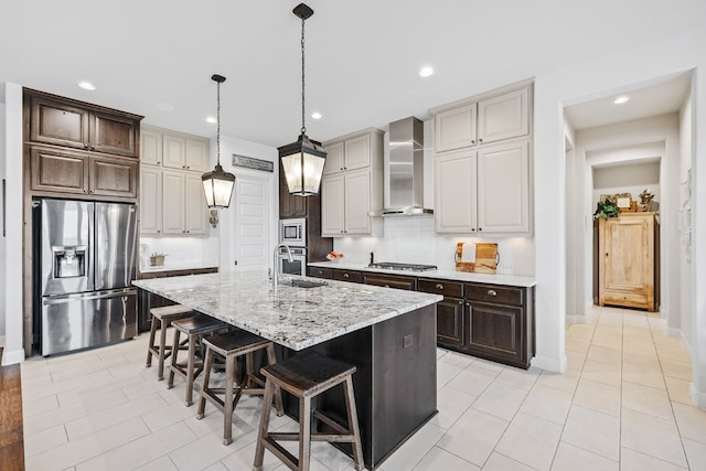 kitchen featuring stainless steel appliances, a kitchen island with sink, wall chimney range hood, light tile patterned floors, and a breakfast bar area