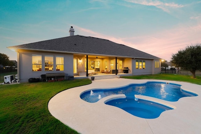 pool at dusk with an in ground hot tub, ceiling fan, a patio area, and a lawn