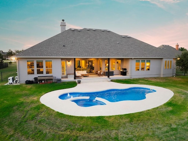 back house at dusk featuring a swimming pool with hot tub, an outdoor hangout area, a patio, and a lawn