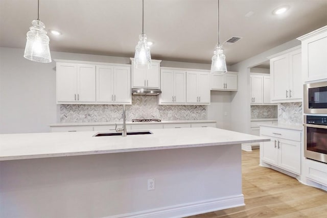 kitchen with pendant lighting, white cabinets, light wood-type flooring, and appliances with stainless steel finishes