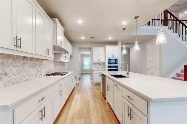 kitchen with stainless steel appliances, white cabinetry, sink, and hanging light fixtures