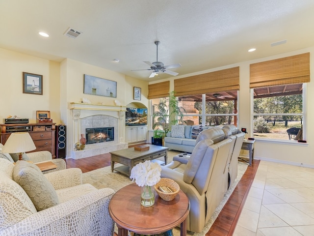 living room featuring ceiling fan, a textured ceiling, light hardwood / wood-style floors, and a tile fireplace