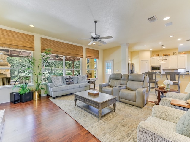 living room featuring ceiling fan, a textured ceiling, light hardwood / wood-style flooring, and ornate columns