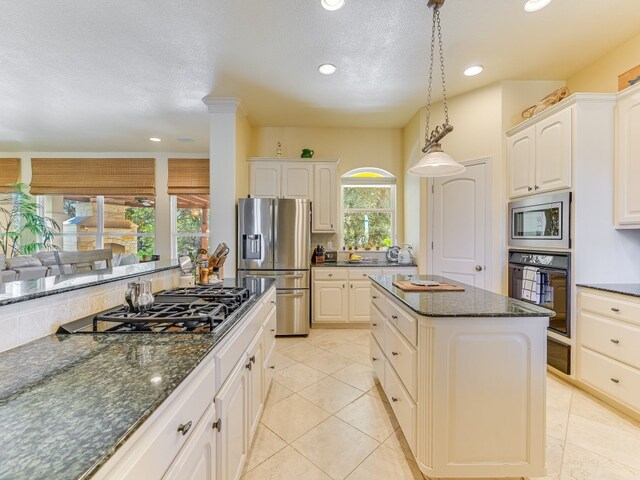 kitchen with white cabinets, decorative light fixtures, appliances with stainless steel finishes, a center island, and dark stone counters