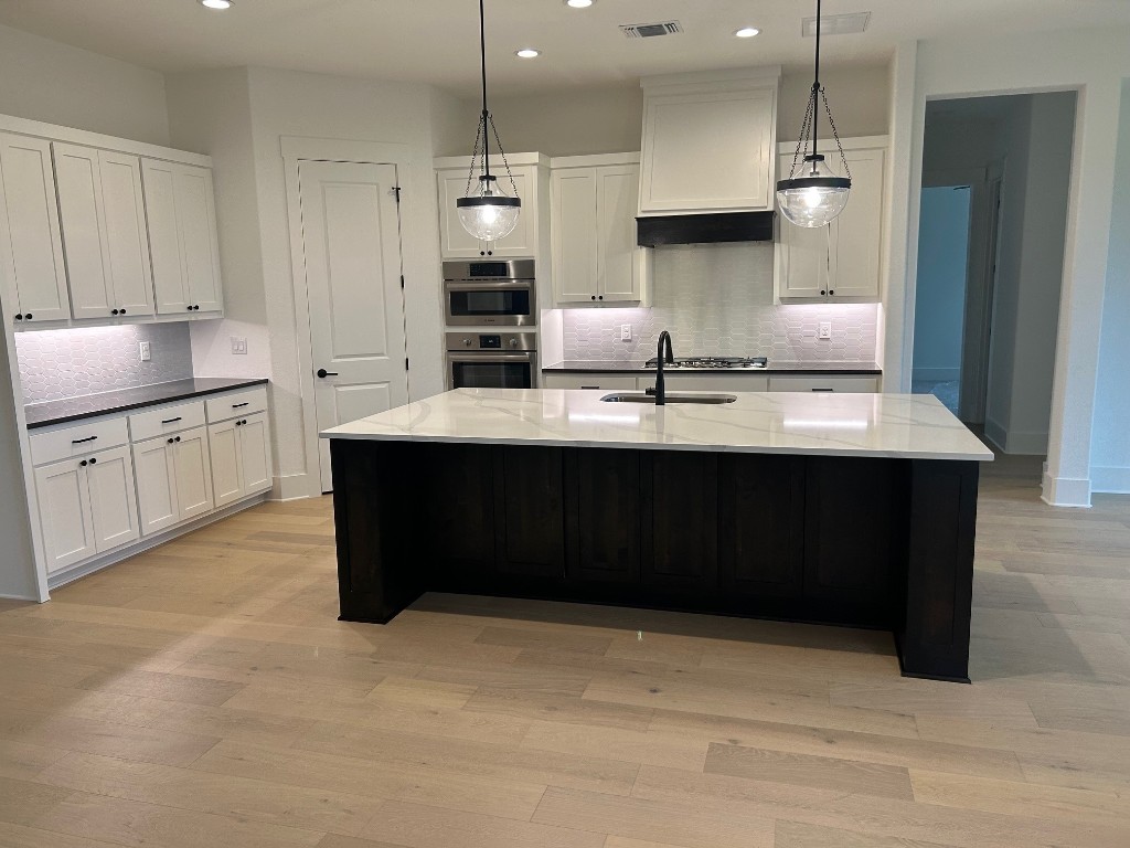 kitchen with a center island with sink, white cabinetry, sink, and decorative light fixtures