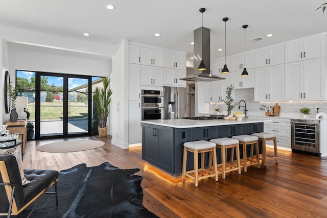 kitchen with a kitchen island, white cabinets, beverage cooler, pendant lighting, and island exhaust hood