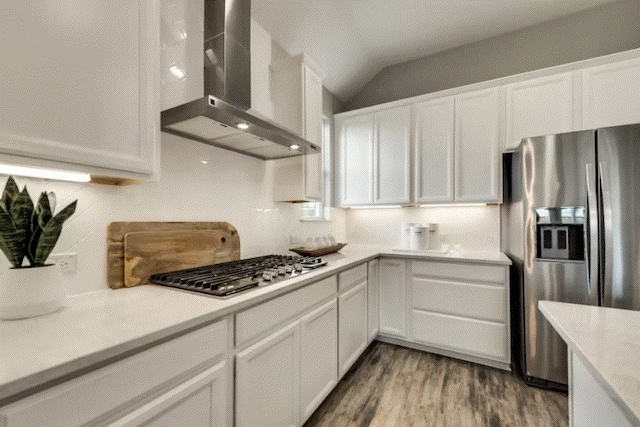 kitchen with wall chimney exhaust hood, light wood-type flooring, vaulted ceiling, stainless steel appliances, and white cabinetry