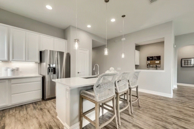 kitchen featuring hanging light fixtures, light hardwood / wood-style floors, stainless steel fridge with ice dispenser, and white cabinetry