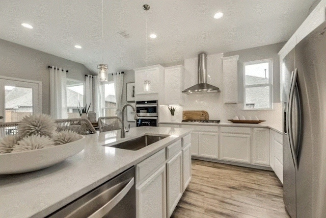 kitchen featuring stainless steel appliances, white cabinets, wall chimney exhaust hood, sink, and pendant lighting