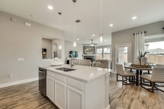 kitchen with white cabinets, sink, stainless steel dishwasher, a kitchen island with sink, and hardwood / wood-style floors