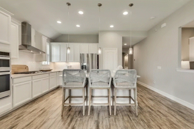 kitchen with white cabinets, appliances with stainless steel finishes, wall chimney range hood, and a center island