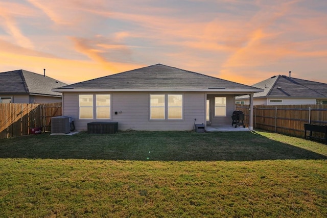 back house at dusk featuring a yard, central AC, and a patio area