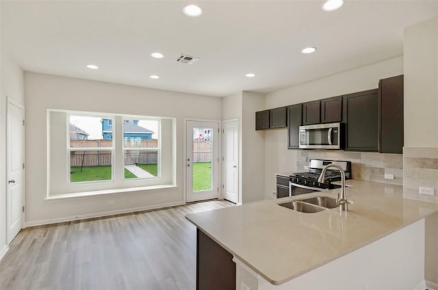 kitchen featuring appliances with stainless steel finishes, sink, light wood-type flooring, dark brown cabinets, and kitchen peninsula