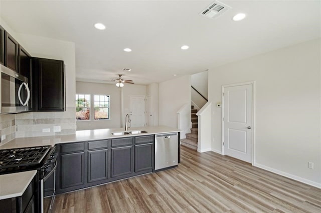 kitchen featuring kitchen peninsula, stainless steel appliances, sink, light hardwood / wood-style floors, and tasteful backsplash