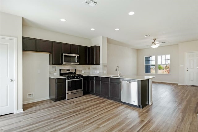 kitchen featuring kitchen peninsula, tasteful backsplash, appliances with stainless steel finishes, light hardwood / wood-style flooring, and sink