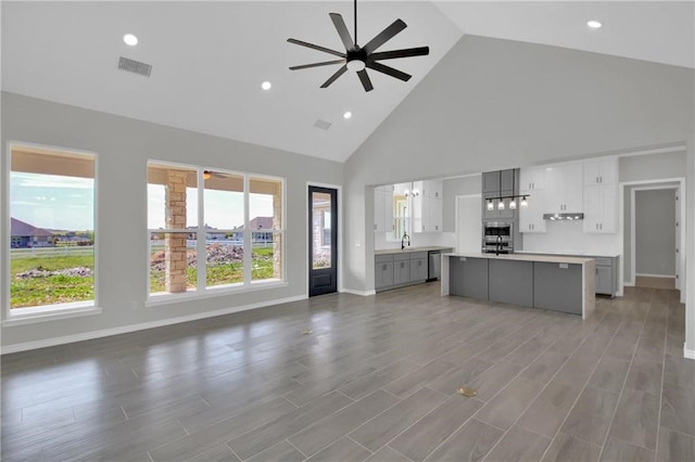unfurnished living room featuring ceiling fan, a sink, baseboards, visible vents, and high vaulted ceiling