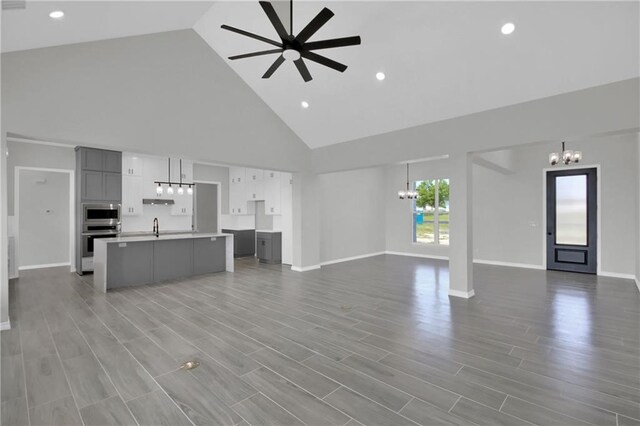 unfurnished living room with a sink, baseboards, wood finished floors, high vaulted ceiling, and ceiling fan with notable chandelier
