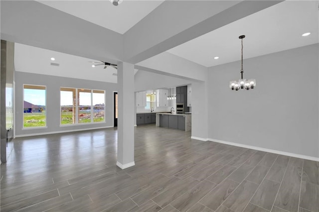 unfurnished living room featuring ceiling fan with notable chandelier and hardwood / wood-style flooring