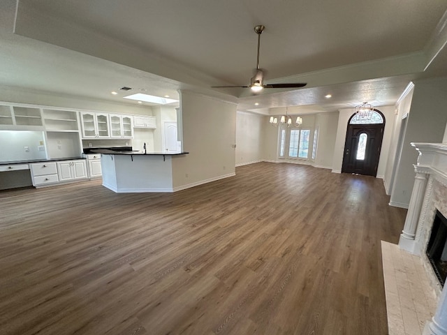 unfurnished living room featuring dark wood-type flooring, ceiling fan with notable chandelier, and crown molding