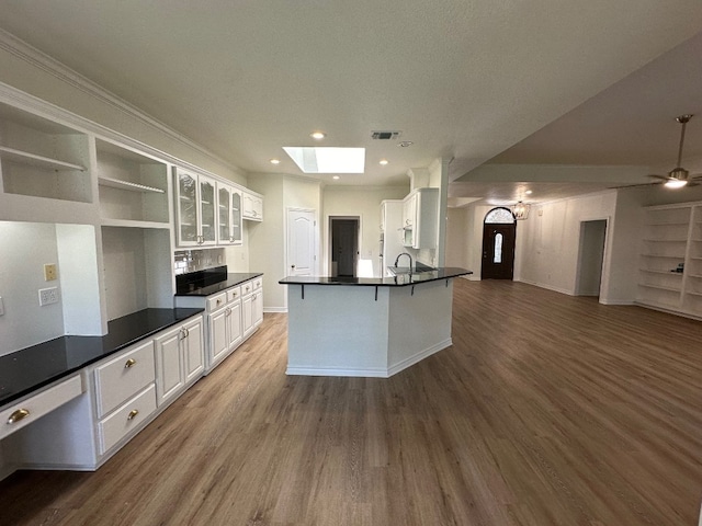 kitchen featuring a skylight, ceiling fan, wood-type flooring, and white cabinets