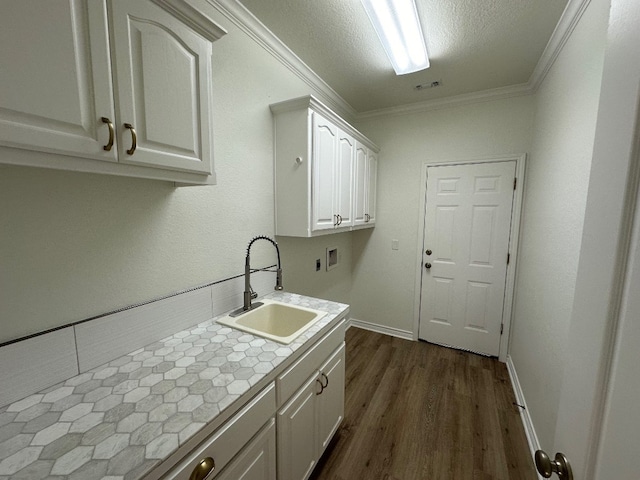 clothes washing area featuring ornamental molding, sink, dark hardwood / wood-style floors, and cabinets