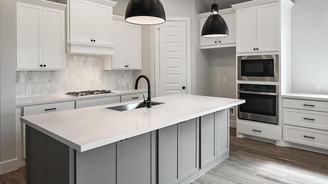 kitchen featuring stainless steel appliances, a sink, light wood-type flooring, backsplash, and an island with sink