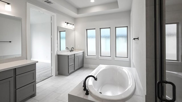 bathroom with baseboards, visible vents, a garden tub, a tray ceiling, and vanity