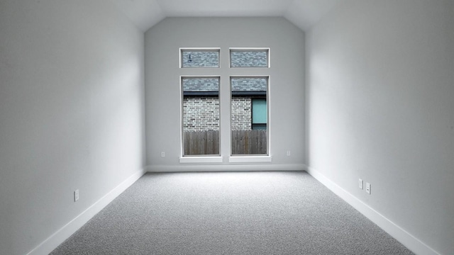 spare room featuring lofted ceiling, baseboards, and carpet flooring