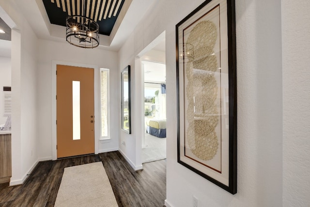 entrance foyer with dark wood-type flooring, a tray ceiling, and a notable chandelier