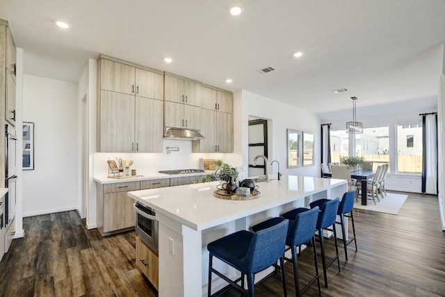 kitchen featuring pendant lighting, light brown cabinetry, a kitchen breakfast bar, dark wood-type flooring, and an island with sink