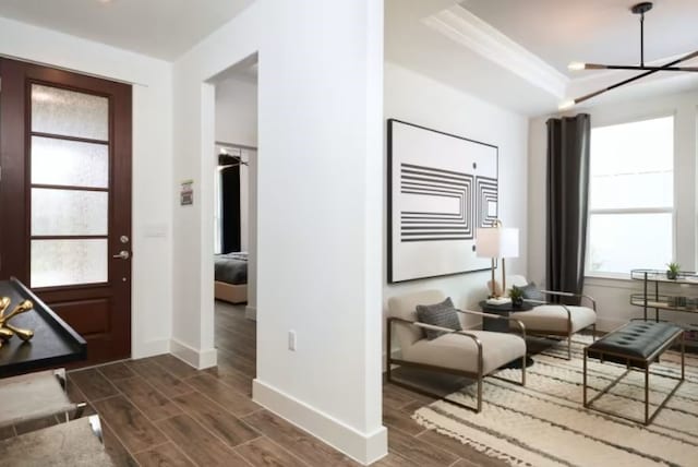 foyer with dark wood-type flooring, a raised ceiling, crown molding, and a chandelier