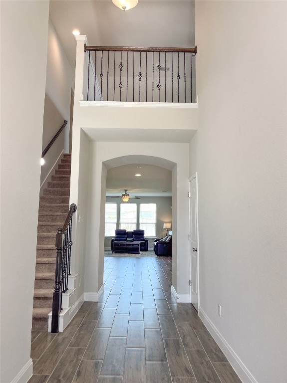 entryway with ceiling fan, a towering ceiling, and wood-type flooring