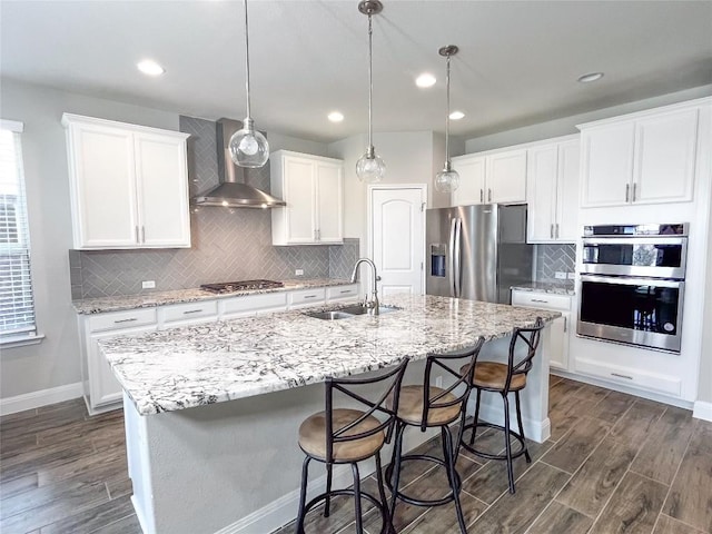 6008 Genova Pl, Round Rock, TX 78665 - kitchen featuring wall chimney exhaust hood, appliances with stainless steel finishes, an island with sink, dark wood finished floors, and recessed lighting