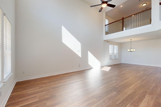 unfurnished living room featuring ceiling fan with notable chandelier, a towering ceiling, and hardwood / wood-style flooring