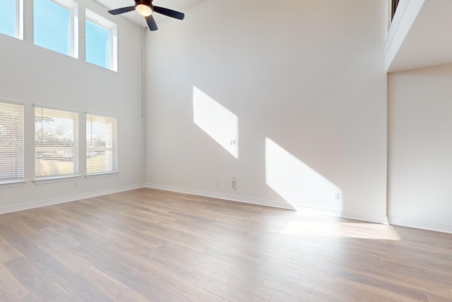 unfurnished living room with ceiling fan, light wood-type flooring, and a high ceiling