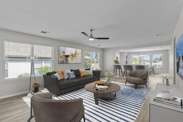 living room with ceiling fan with notable chandelier, light hardwood / wood-style flooring, and plenty of natural light