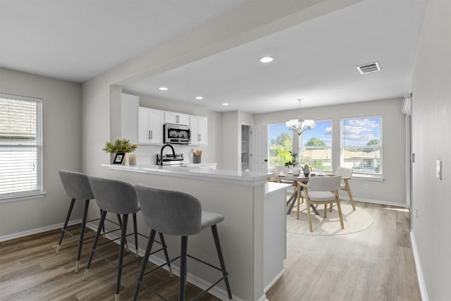 kitchen featuring white cabinets, pendant lighting, kitchen peninsula, a chandelier, and light wood-type flooring