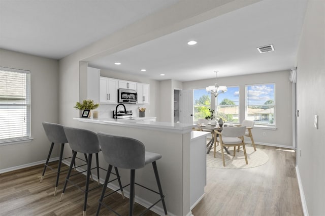 208 Bright Leaf Trl, Georgetown, TX 78633 - kitchen featuring stainless steel microwave, baseboards, a peninsula, a chandelier, and light wood-style flooring