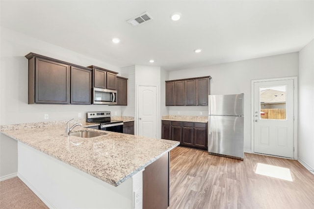 kitchen with appliances with stainless steel finishes, sink, light wood-type flooring, dark brown cabinets, and kitchen peninsula