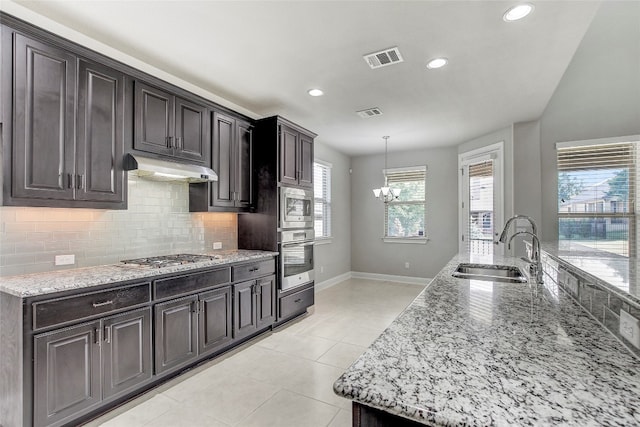 kitchen featuring dark brown cabinetry, sink, light stone counters, decorative light fixtures, and appliances with stainless steel finishes