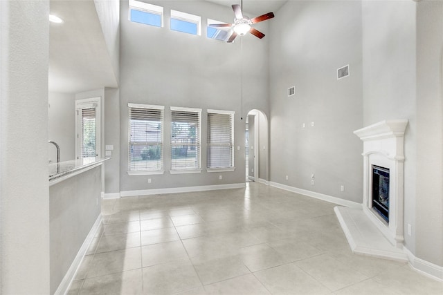 unfurnished living room with ceiling fan, a towering ceiling, and light tile patterned floors