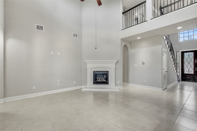 unfurnished living room featuring ceiling fan, a towering ceiling, and light tile patterned floors