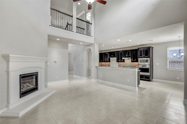 unfurnished living room with ceiling fan, light tile patterned floors, and a towering ceiling