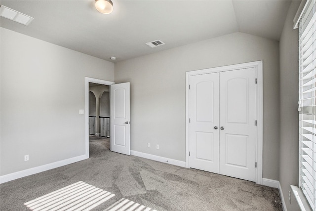 unfurnished bedroom featuring light colored carpet, lofted ceiling, and a closet