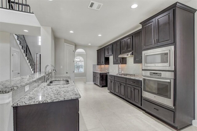 kitchen featuring sink, tasteful backsplash, light stone counters, dark brown cabinets, and appliances with stainless steel finishes